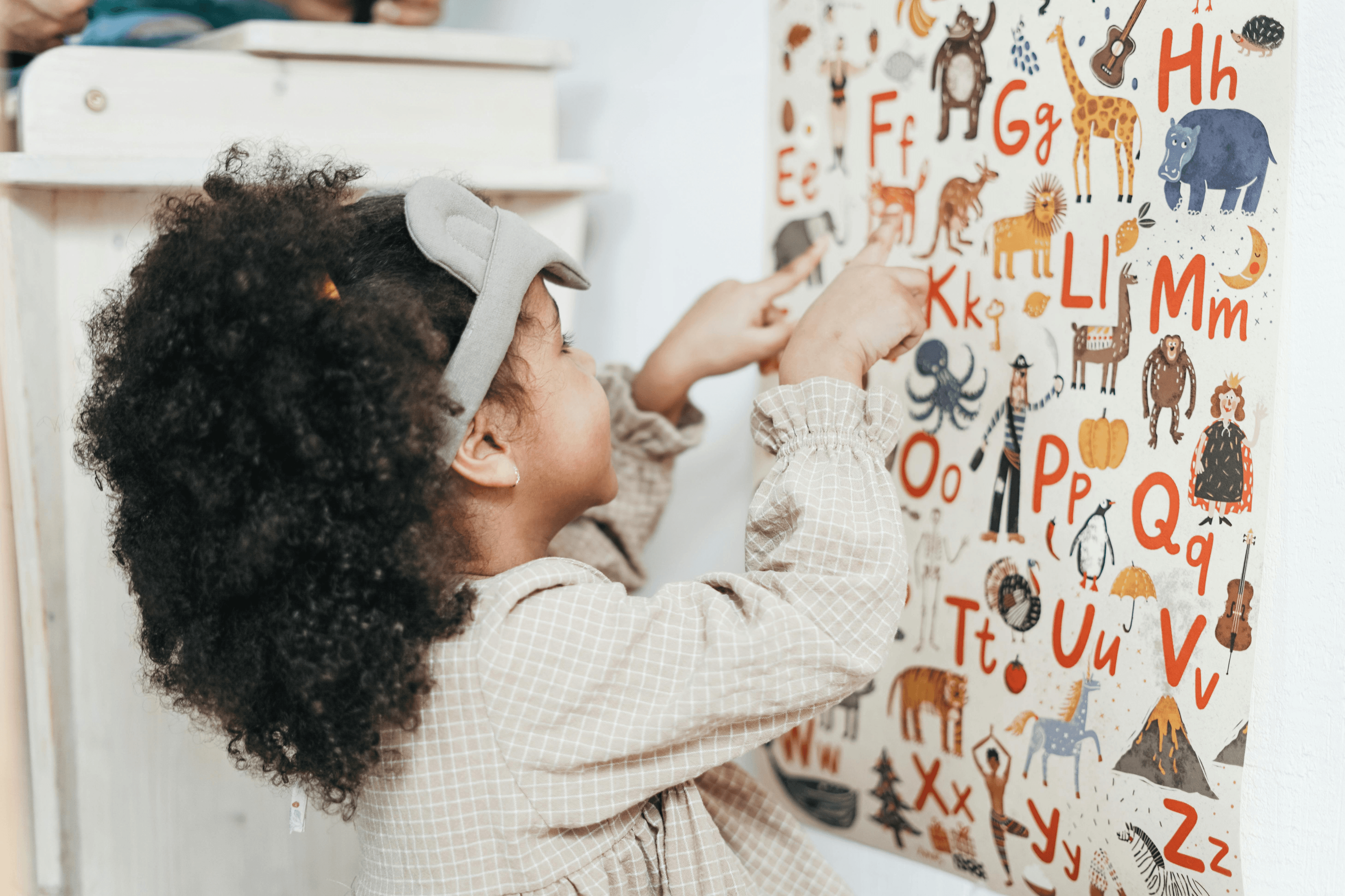 Young girl pointing to animals on Alphabet poster